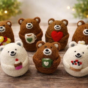 May include: A collection of handmade felt bear figurines in various shades of brown and white. Some bears hold a heart, flowers, a cup of coffee, or a cupcake. The bears have smiling faces and are arranged on a wooden surface.
