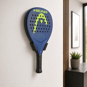 May include: A blue and black Head Zephyr paddleball racket mounted on a wall. The racket has a neon green logo and the word "HEAD" at the top. The handle is black and the racket is held in place by a black wall mount.