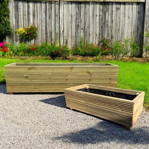 May include: Two rectangular wooden planters with a slatted design. The larger planter is in the background, and the smaller one is in the foreground. Both planters are empty and sit on small wooden feet. The planters are made of light-coloured wood.