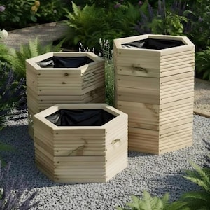 May include: Three hexagonal planters constructed from light-coloured horizontal wooden slats. Each planter features a black interior liner and a distinct height, with two shorter units positioned in the front and one taller unit located in the back.