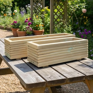 May include: Two rectangular planters constructed from light-coloured horizontal wooden slats. Each planter features a clean, open-top design with visible metal fasteners at the corners, providing a sturdy structure for holding plants or floral arrangements.