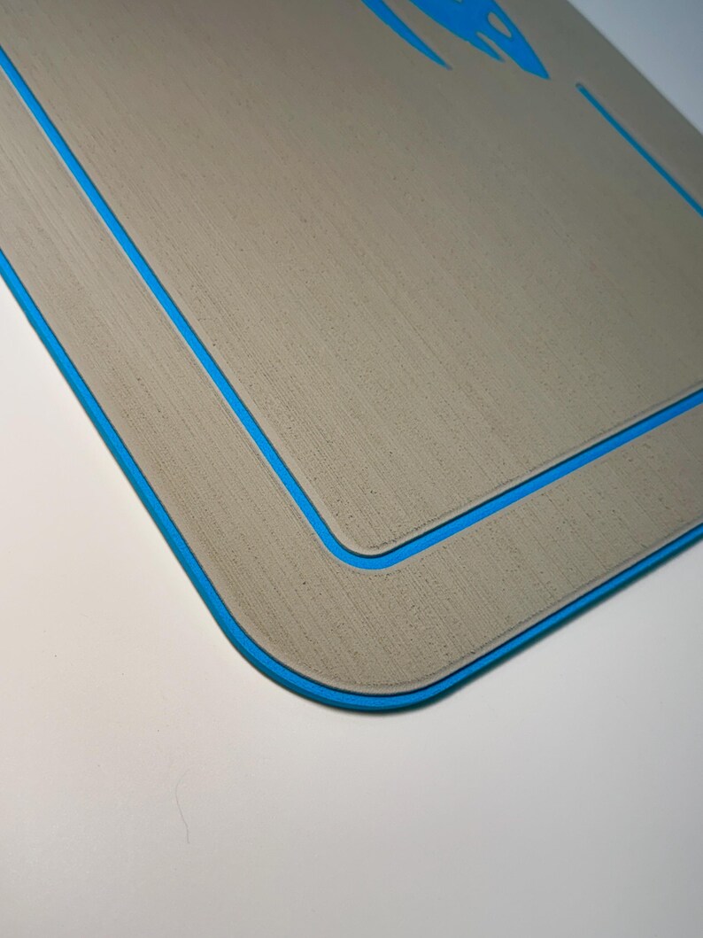 May include: A rectangular, light gray mat with a blue border. The mat has a textured surface and a blue design in the upper corner. The edges are rounded, and the mat is set against a white background.