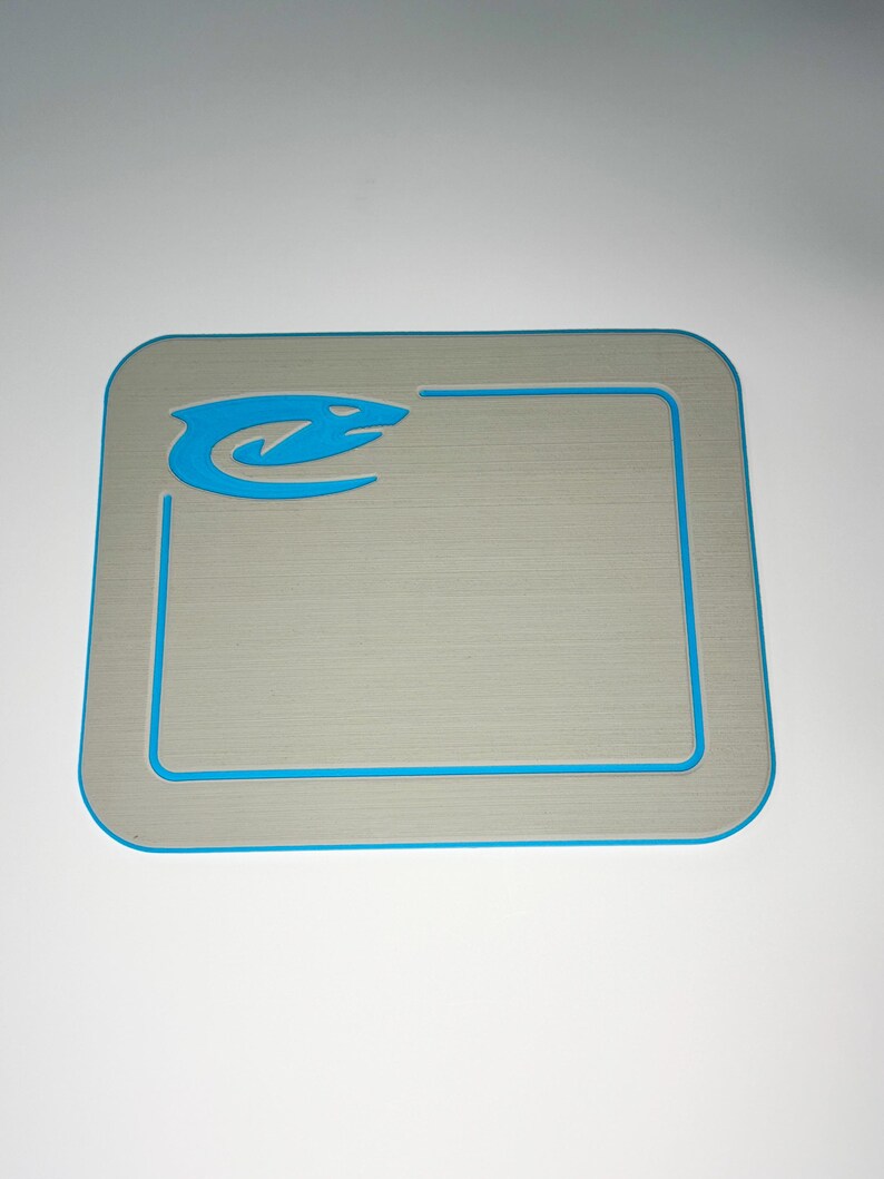 May include: A rectangular, gray mat with a blue border and a blue stylized snake logo in the upper left corner. The mat has a textured surface and rounded corners. The border is a thin, bright blue line.