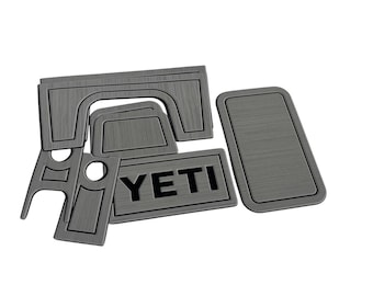 Könnte beinhalten: Ein Set aus dunkelgrauen Innenraum-Verkleidungsteilen mit gebürsteter Metalloptik für eine Fahrzeugkonsole. Die Teile haben präzise Aussparungen für Knöpfe und Regler, wobei ein rechteckiges Element den schwarzen Schriftzug YETI trägt.