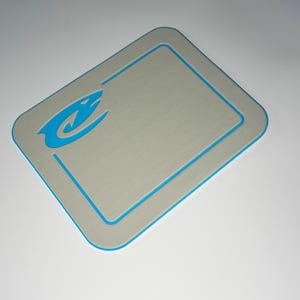 May include: A rectangular gray mat with a blue border and a blue logo in the upper left corner. The logo is a stylized image of a shark. The mat has rounded corners.