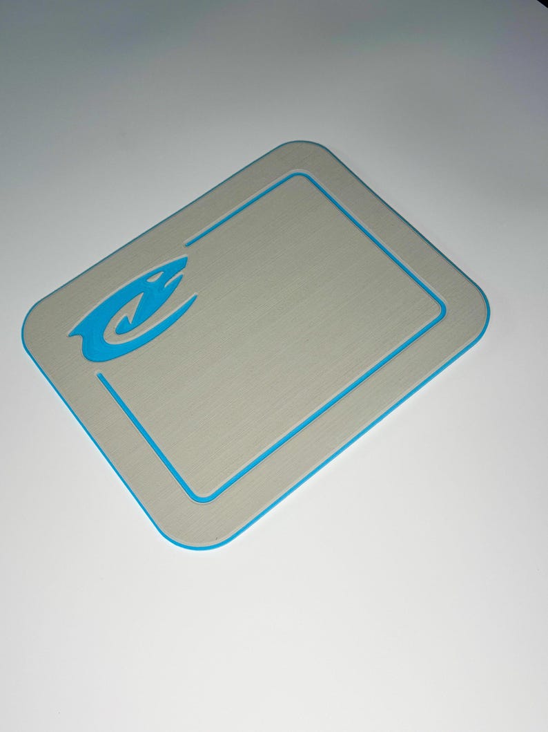 May include: A rectangular gray mat with a blue border and a blue logo in the upper left corner. The logo is a stylized image of a shark. The mat has rounded corners.