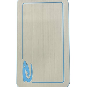 Puede incluir: Un objeto rectangular de color claro con un borde azul y un dise&ntilde;o de llama azul estilizado en la esquina. La superficie tiene una textura de vetas de madera. El objeto es probablemente un elemento decorativo o funcional.