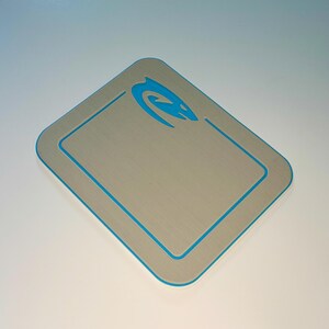 May include: A silver-colored digital scale with a blue trim and a blue logo in the upper right corner. The scale has a rectangular shape with rounded corners. The scale is designed for measuring weight.