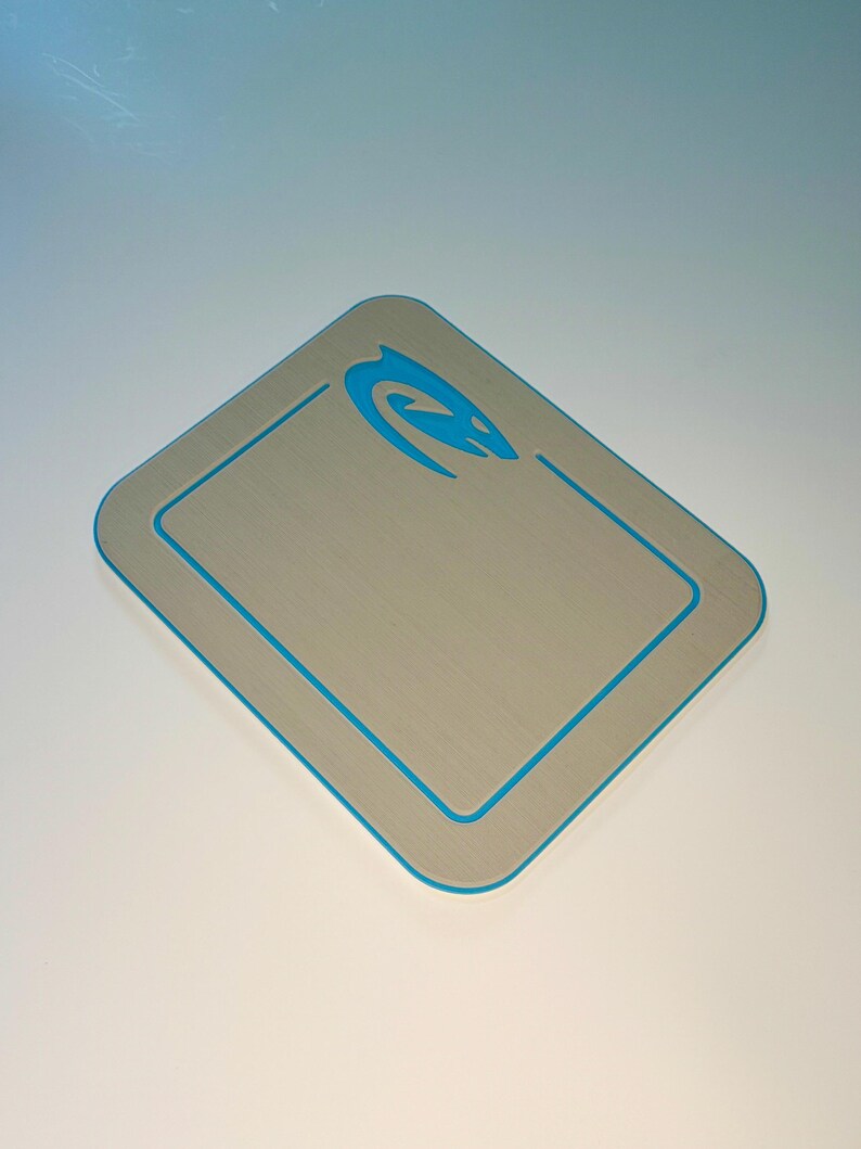 May include: A silver-colored digital scale with a blue trim and a blue logo in the upper right corner. The scale has a rectangular shape with rounded corners. The scale is designed for measuring weight.