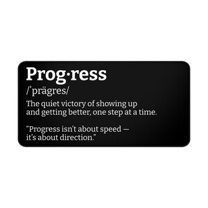 Puede incluir: Un letrero rectangular negro con esquinas redondeadas presenta la palabra "Progress" en blanco, junto con su pronunciación. Debajo, el texto define el progreso como la victoria silenciosa de presentarse y mejorar, paso a paso. También se incluye una cita sobre la dirección.