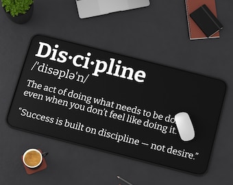 Könnte beinhalten: Schwarze rechteckige Schreibtischunterlage mit dem Wort "Disziplin" in Weiß, zusammen mit seiner Aussprache und einer Definition. Eine weiße Maus, eine Tasse Kaffee, ein Laptop und eine kleine Pflanze sind ebenfalls sichtbar.