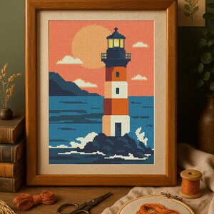 May include: Framed cross-stitch art featuring a lighthouse on a rocky island, with a sunset backdrop. The lighthouse is white, orange, and blue. The artwork is in a wooden frame. The image also includes craft supplies like thread and scissors.