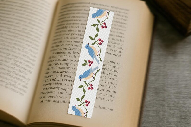 Cross stitch bookmark with blue birds and berries on vintage book, finished embroidery project