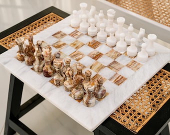 Può includere: Un set di scacchi con una scacchiera quadrata a riquadri alternati in marmo bianco e onice marrone. Il set include sedici pezzi degli scacchi in marmo bianco massiccio e sedici in onice marrone con venature naturali, disposti nelle posizioni iniziali.