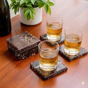 Pu&ograve; includere: Un set di sottobicchieri quadrati in marmo marrone scuro e bianco con finitura lucida. Due bicchieri trasparenti riempiti con un liquido ambrato dorato sono posizionati su singoli sottobicchieri, mentre una pila di tre sottobicchieri extra &egrave; vicina.
