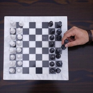 Pu&ograve; includere: Una scacchiera quadrata caratterizzata da una griglia di quadrati in marmo bianco e nero alternati. La scacchiera &egrave; disposta con un set completo di pezzi degli scacchi in marmo bianco da un lato e pezzi in marmo nero dall'altro lato.