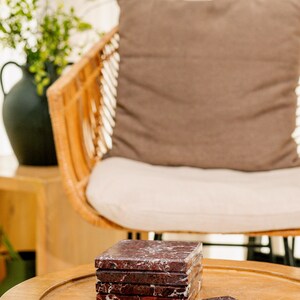 Pu&ograve; includere: Un set di cinque sottobicchieri quadrati in marmo rosso scuro con venature bianche prominenti. Quattro sottobicchieri sono impilati in una colonna verticale, mentre un singolo sottobicchiere &egrave; appoggiato in piano sulla superficie davanti alla pila, mostrando la texture della pietra.