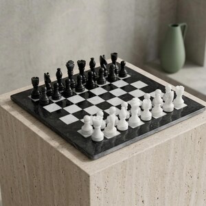 Pu&ograve; includere: Una scacchiera quadrata con caselle alternate in marmo bianco e nero. La scacchiera presenta un set completo di pezzi degli scacchi intagliati in marmo bianco e nero, disposti nelle loro posizioni iniziali sulla superficie del piano di gioco.