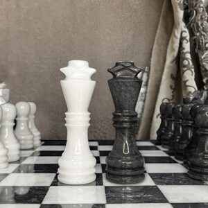 Pu&ograve; includere: Un pezzo degli scacchi re in marmo bianco e un pezzo degli scacchi re in marmo nero affiancati su una scacchiera in marmo bianco e nero abbinata. I pezzi presentano una finitura liscia e lucida con un terminale a forma di croce in cima.