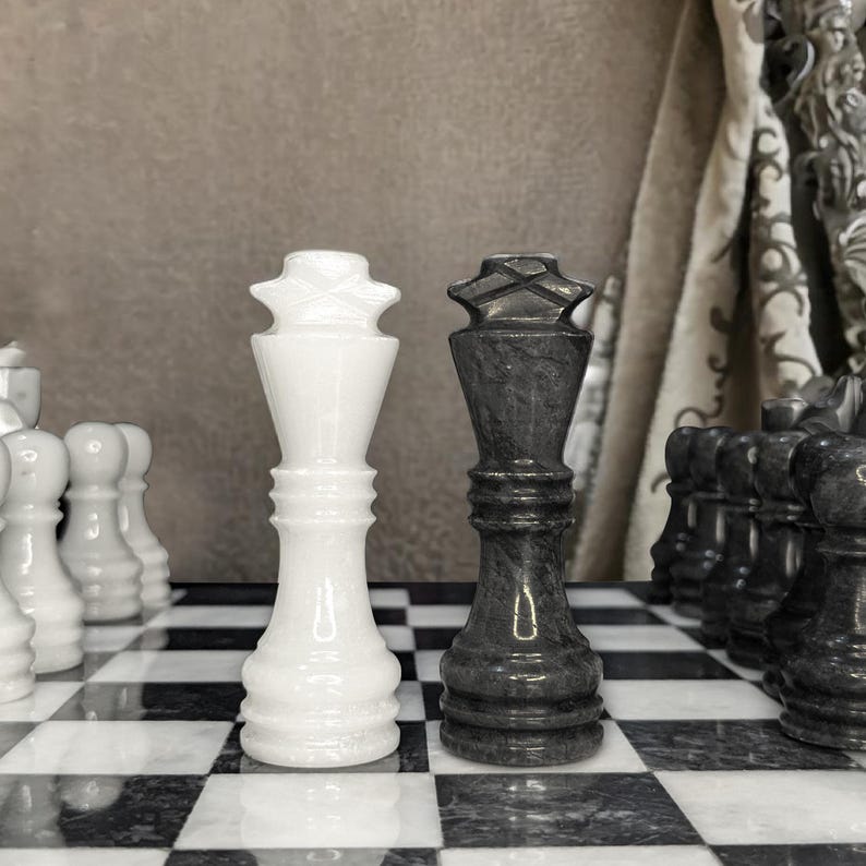 Pu&ograve; includere: Un pezzo degli scacchi re in marmo bianco e un pezzo degli scacchi re in marmo nero affiancati su una scacchiera in marmo bianco e nero abbinata. I pezzi presentano una finitura liscia e lucida con un terminale a forma di croce in cima.