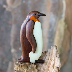 Könnte beinhalten: Eine hölzerne Pinguinfigur, die braun und weiß bemalt ist. Der Pinguin steht auf einem Stück Treibholz.