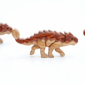 Three handmade wooden ankylosaur dinosaur Christmas ornaments or magnets made using the segmented wood artform of intarsia.