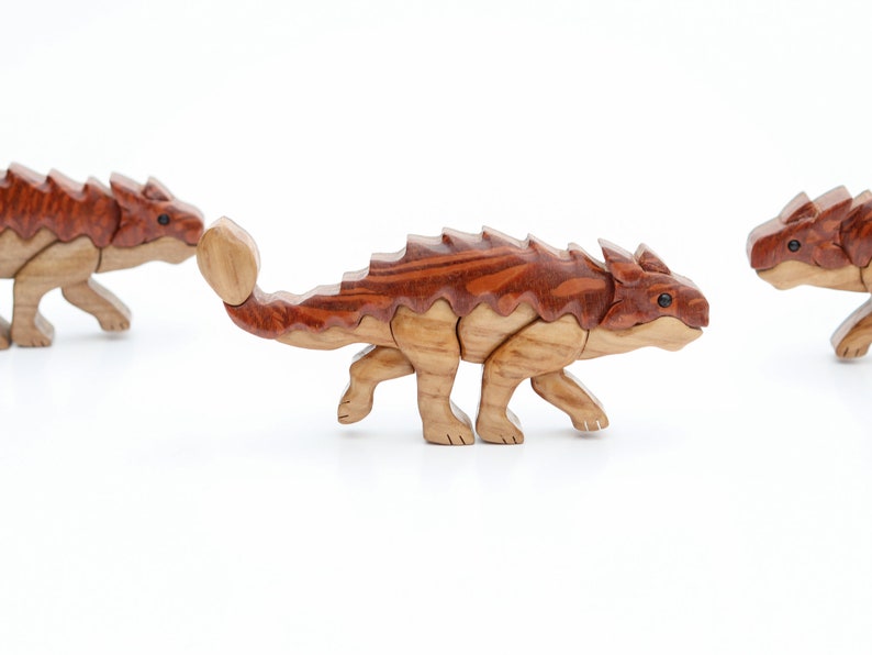 Three handmade wooden ankylosaur dinosaur Christmas ornaments or magnets made using the segmented wood artform of intarsia.