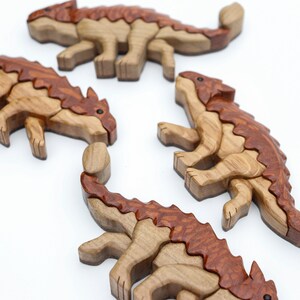 A group os handmade wooden ankylosaur dinosaur Christmas ornaments or magnets made using the segmented wood artform of intarsia. All are laying down flat.