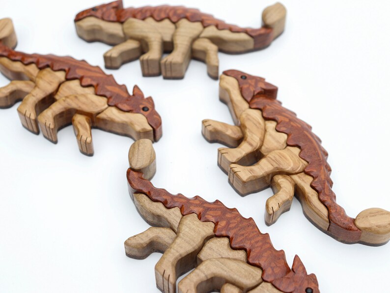 A group os handmade wooden ankylosaur dinosaur Christmas ornaments or magnets made using the segmented wood artform of intarsia. All are laying down flat.