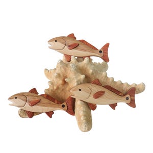 May include: Wooden sculpture featuring three fish with reddish-brown fins and tails, resting on a beige starfish. The fish are crafted from light and dark wood, creating a natural, nautical theme.