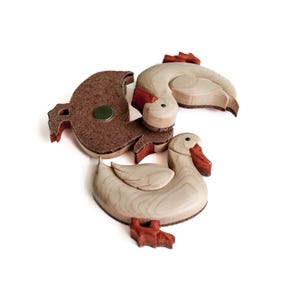 Pode incluir: Tr&ecirc;s ornamentos de madeira em forma de pato, dois s&atilde;o brancos com bicos e p&eacute;s laranja, um &eacute; castanho com um &iacute;man na parte de tr&aacute;s.