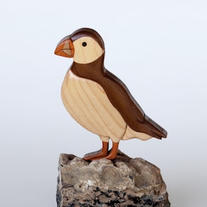 May include: A wooden carving of a puffin standing on a rock. The puffin is brown and white with an orange beak. The rock is gray and brown.