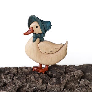 Pode incluir: Uma figura de pato de madeira com um chap&eacute;u azul e uma gravata borboleta azul. O pato est&aacute; em p&eacute; em um peda&ccedil;o de casca de &aacute;rvore.