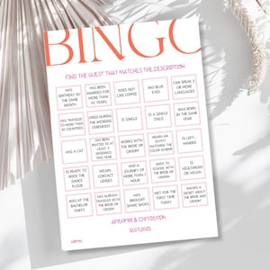 May include: A white Bingo game card with coral text and a decorative border. The card features a grid of descriptive phrases for guests to match, such as "Has blue eyes" and "Was born in the same year." The card is for a wedding.