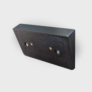 Könnte beinhalten: Eine schwarze, abgewinkelte Wandhalterung mit strukturierter Oberfläche. Die Halterung hat vorgebohrte Löcher für Schrauben und eine flache Oberseite. Die Halterung ist für die Wandmontage konzipiert.