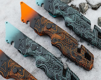 Könnte beinhalten: Utilitymesser mit Farbverlaufklingen in Orange und Türkis, mit einem topografischen Muster auf den Griffen. Die Messer haben einen Flaschenöffner und einen Gurtschneider. Die Klingen sind schwarz mit Farbverlauf.