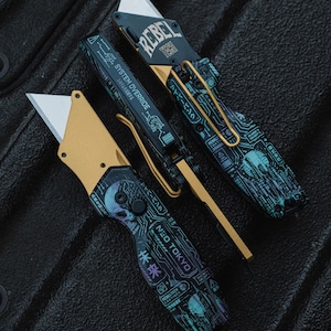 Peut inclure: Deux couteaux utilitaires pliants avec des accents dorés métalliques et des manches noirs ornés de motifs de circuits imprimés bleu sarcelle. L'un porte le texte REBEL TECH et SYSTEM OVERRIDE, l'autre NEO TOKYO et des caractères japonais.