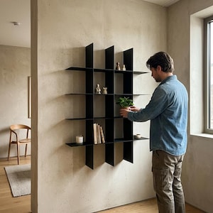 May include: A black metal wall-mounted shelving unit featuring a grid design with multiple open compartments. The structure consists of thin vertical and horizontal panels that create a geometric display area for small decorative objects and plants.
