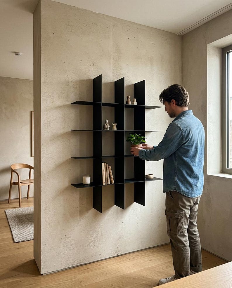 May include: A black metal wall-mounted shelving unit featuring a grid design with multiple open compartments. The structure consists of thin vertical and horizontal panels that create a geometric display area for small decorative objects and plants.