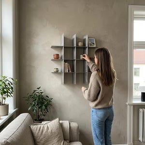 May include: A wall-mounted metal grid shelving unit featuring a series of square compartments. The shelf is constructed from thin, grey vertical and horizontal panels that intersect to create multiple open storage spaces for small decorative items.