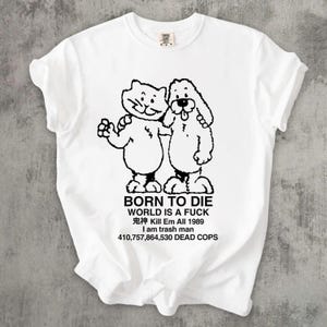 Pode incluir: Camiseta branca com um desenho preto de um gato e um cachorro abra&ccedil;ados, com o texto "BORN TO DIE WORLD IS A FUCK" e outras frases. A camiseta tem gola redonda e mangas curtas.