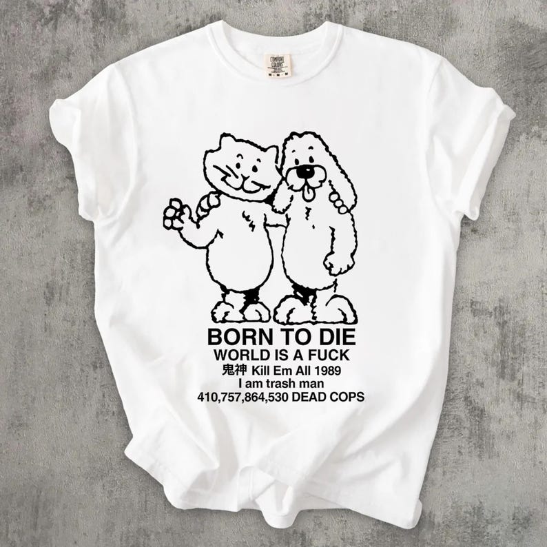 Pode incluir: Camiseta branca com um desenho preto de um gato e um cachorro abra&ccedil;ados, com o texto "BORN TO DIE WORLD IS A FUCK" e outras frases. A camiseta tem gola redonda e mangas curtas.