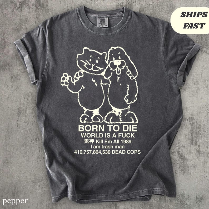 Pode incluir: Camiseta cinza-pimenta com um gr&aacute;fico branco de dois animais de desenho animado e texto. O texto inclui "BORN TO DIE WORLD IS A FUCK" e outras frases. A camiseta tem mangas enroladas.