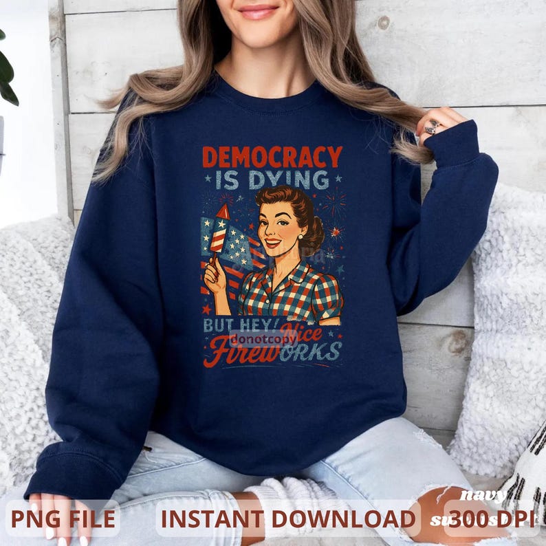 May include: Navy blue sweatshirt featuring a retro-style graphic. The graphic includes the text "DEMOCRACY IS DYING" and "BUT HEY! Fireworks" with an illustration of a woman holding a firework and an American flag.