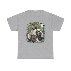 May include: A grey t-shirt with a Halloween graphic. The design features the text "Spells Work Better With Caffeine" alongside illustrations of witches, cats, ghosts, and a cauldron. The shirt is made of a soft, comfortable material.