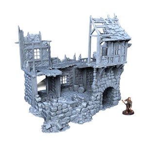 May include: A gray, miniature, ruined medieval building with stone walls, wooden beams, and a tiled roof. The structure has an arched doorway and several windows. A small figurine of a person is standing nearby.