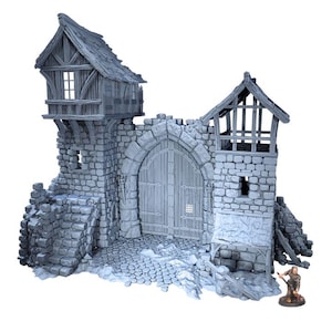 Puede incluir: Una maqueta gris de una puerta de castillo con fachada de piedra, detalles de madera y aspecto envejecido. La puerta presenta una gran entrada arqueada, una peque&ntilde;a figura y un camino empedrado. El castillo tiene dos torres con peque&ntilde;as ventanas y un tejado de madera.
