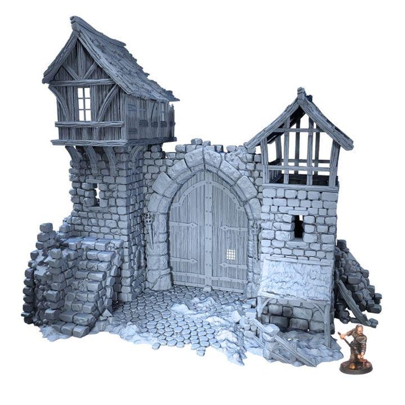 Puede incluir: Una maqueta gris de una puerta de castillo con fachada de piedra, detalles de madera y aspecto envejecido. La puerta presenta una gran entrada arqueada, una peque&ntilde;a figura y un camino empedrado. El castillo tiene dos torres con peque&ntilde;as ventanas y un tejado de madera.