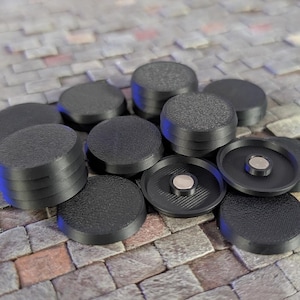 May include: A collection of circular black plastic tokens with a textured top surface. Some tokens are stacked, while others are flipped over to reveal a smooth interior rim and a small, centered circular metal magnet insert.
