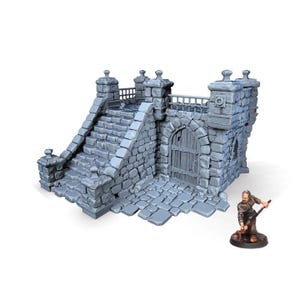May include: A gray stone miniature castle structure with stairs, a gate, and a small figure of a person. The castle has a detailed, textured surface and is designed for tabletop gaming or display.